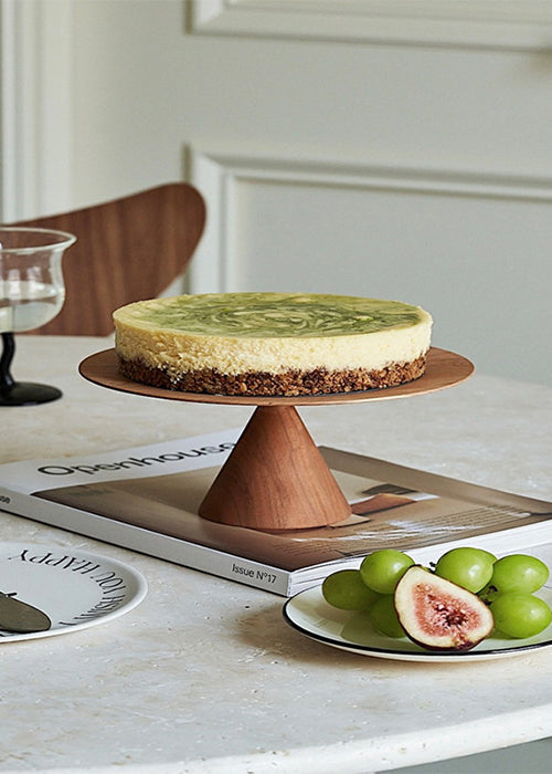A beautifully crafted cake stand made from rich cherry wood. The stand features a cone-shaped base and a flat, disc-shaped top serving as a platform for showcasing delectable cakes. The warm, natural tones of the cherry wood enhance the elegance of this piece, making it an exquisite addition to your dessert presentation and a perfect complement to any occasion