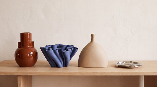 Three ceramic vases and a chrome tray styled on an oak console, in cognac, indigo and matte beige