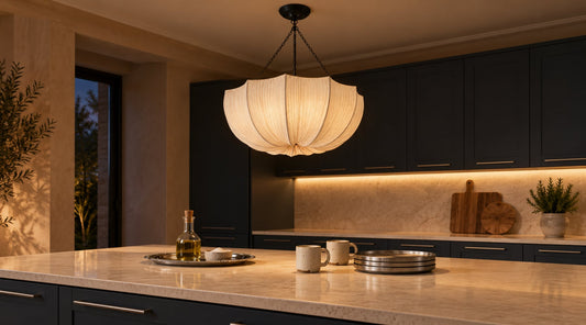 Dark charcoal kitchen with a pale stone island lit by a gathered fabric pendant, with brushed steel tableware and speckled stoneware mugs