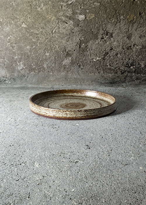 Handmade stone plate, measuring W22cm x H2.5cm. Exhibiting a rugged yet sleek style, this plate is part of a comprehensive set of raw pottery dishes and mugs designed for versatile dining needs.